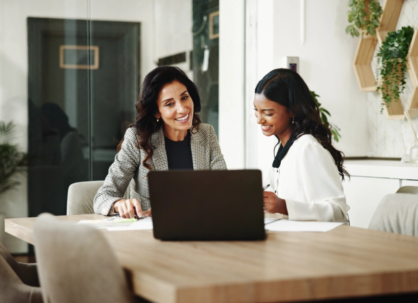 Two women engaged in a friendly discussion over a laptop.