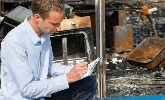 Man inspecting fire damage and taking notes on clipboard.