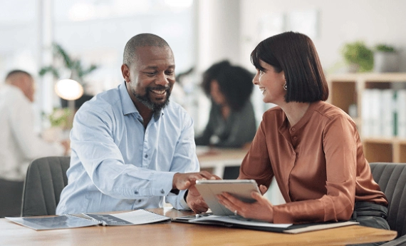 Two colleagues discussing work on a tablet in a bright office.