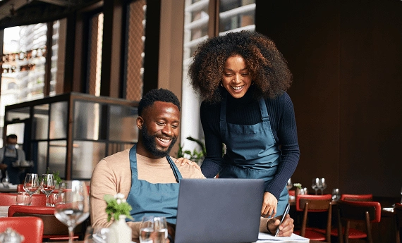Two happy baristas working together at a laptop in a café.